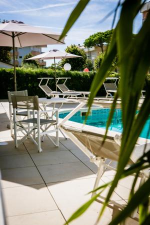 Piscina all'aperto con lettini e ombrelloni, circondata da vegetazione.