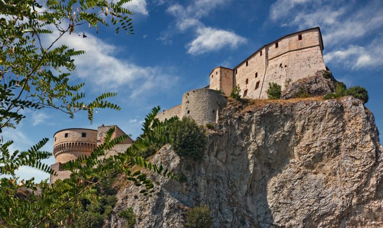 Castello medievale su una scogliera con cielo blu e nuvole.