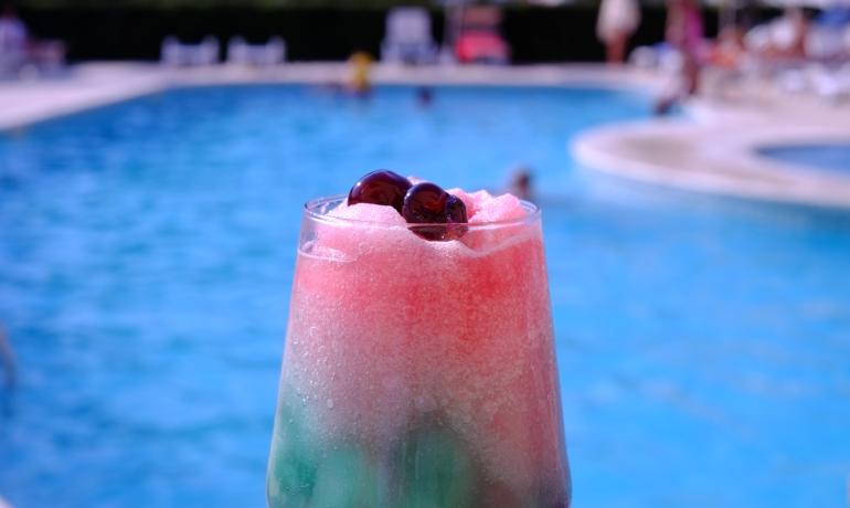 Cocktail colorato con ciliegie vicino a una piscina.