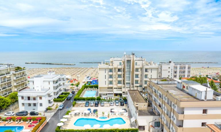 Vista panoramica su hotel, piscine e spiaggia con mare sullo sfondo.