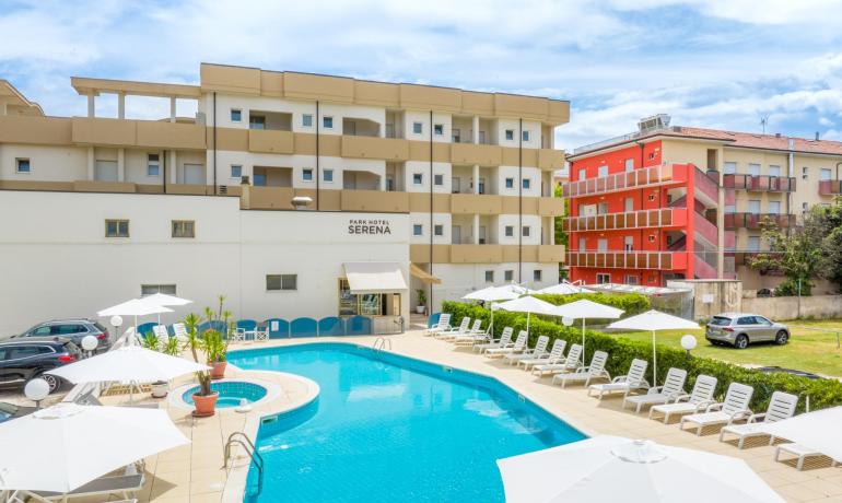 Hotel con piscina all'aperto, lettini e ombrelloni, cielo sereno.