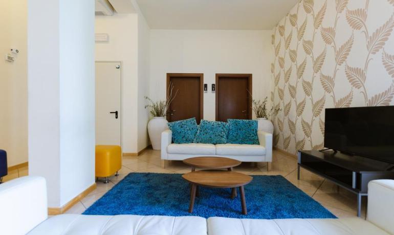 Modern living room with white sofas, blue rug, and decorative wallpaper.